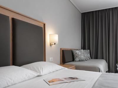 Modernes Schlafzimmer mit zwei Betten, grauen Vorhängen, Wandlampe und einem kleinen Tisch mit Blumen.