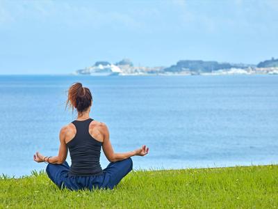 Kobieta medytująca nad morzem na zielonej trawie z widokiem na odległe wyspy.