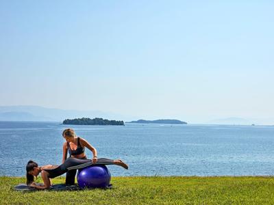 Dwie kobiety rozciągające się z piłką fitness nad brzegiem jeziora na zielonej trawie