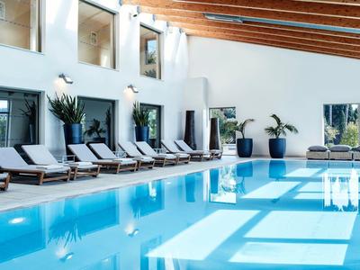 Moderner Innenpool mit Liegestühlen, großen Fenstern und Holzdecke in hellem, offenen Raum.