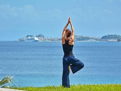Kobieta ćwicząca jogę na trawniku z widokiem na niebieskie morze i odległą wyspę.