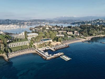 Luftaufnahme einer Küstenstadt mit Hafen, grünen Hügeln und mehreren Gebäuden am Meer.