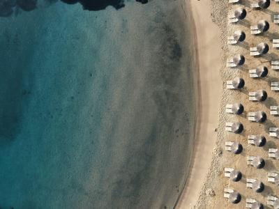 Luftaufnahme eines Strandes mit klarem blauem Wasser und Reihen von Sonnenschirmen auf hellem Sand.