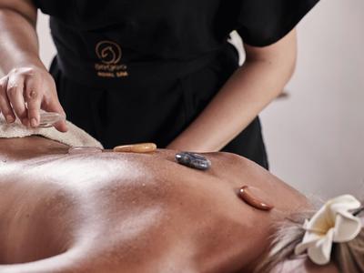 Eine Person erhält eine Massage, der Rücken ist mit heißen Steinen bedeckt, die Haut glänzt.