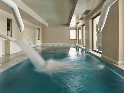 Innenpool mit Wasserfontänen, großen Fenstern und hellen Wänden in modernem Design.