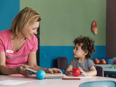 Eine Frau und ein Kind sitzen an einem Tisch und spielen mit bunten Kugeln und Holzbrett.