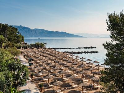 Rząd pustych leżaków z parasolami na plaży nad spokojnym morzem, w tle góry.