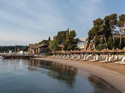 Plaża z leżakami i parasolami przed hotelem i drzewami pod niebieskim niebem