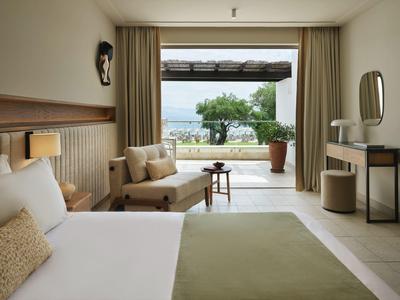 Modernes Hotelzimmer mit großem Bett, Sitzbereich und Blick auf Terrasse mit Baum und Landschaft.