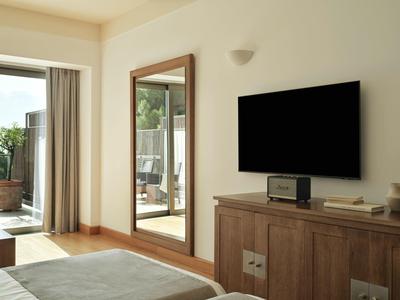 Moderner Hotelzimmerbereich mit TV, großem Spiegel und Zugang zum Balkon mit Pflanzen.