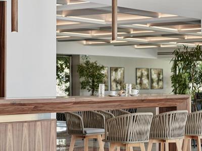 Moderner Hotelbarbereich mit Holz und Rattanstühlen unter geometrischer Deckenbeleuchtung.