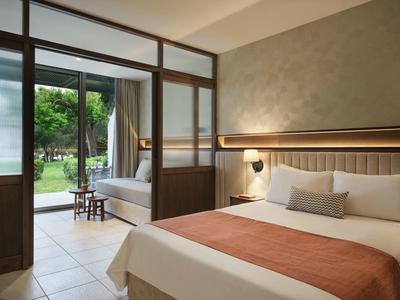 Modernes Hotelzimmer mit Doppelbett, Sitzecke und Blick auf einen Garten mit Teich.