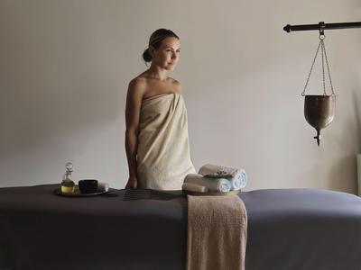 Žena v ručníku stojí vedle masážního stolu v klidné spa místnosti.