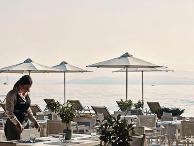 Terasa restaurace s deštníky u klidného moře, servírka připravuje stoly.