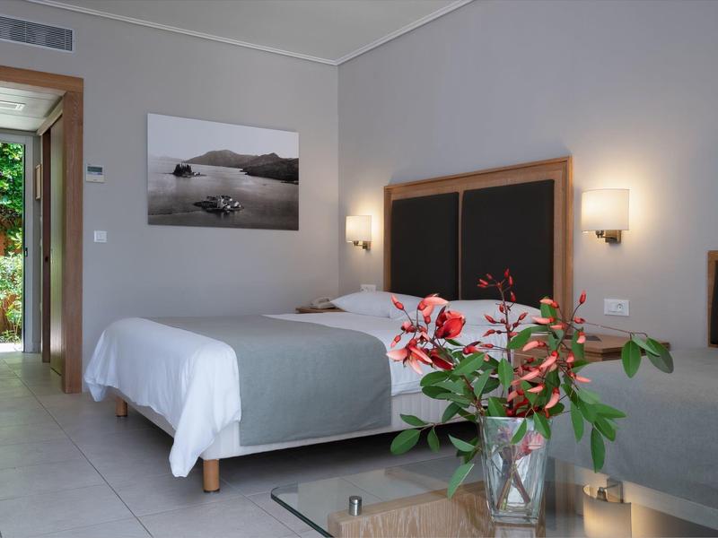 Helles Schlafzimmer mit Doppelbett, grauer Bettwäsche, Pflanzen und offenem Blick auf einen Garten.