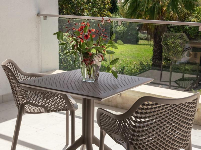 Moderner Balkon mit grauem Tisch, zwei geflochtenen Stühlen und Blumenstrauß im Glasvase.
