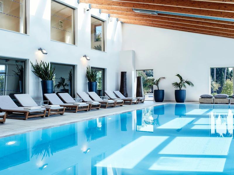 Moderner Innenpool mit Liegestühlen, großen Fenstern und Holzdecke in hellem, offenen Raum.