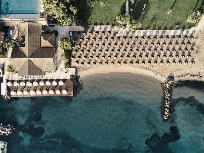 Strand mit Liegestühlen, Sonnenschirmen und einem Holzsteg neben klarem blauem Wasser.
