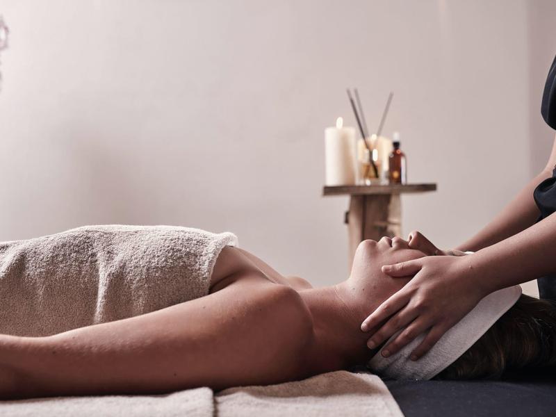 Frau erhält entspannende Gesichtsmassage in ruhigem, sanft beleuchtetem Wellnessraum mit Kerzen.