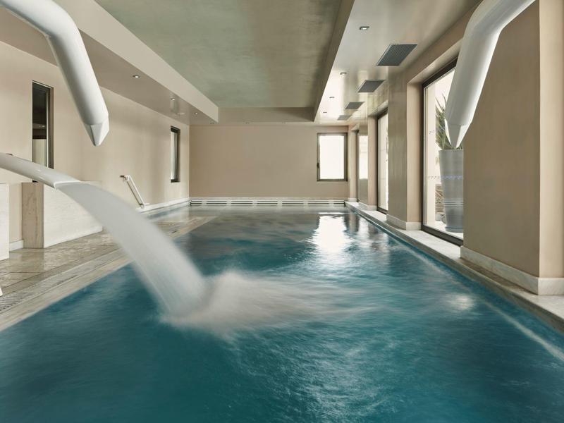 Innenpool mit Wasserfontänen, großen Fenstern und hellen Wänden in modernem Design.