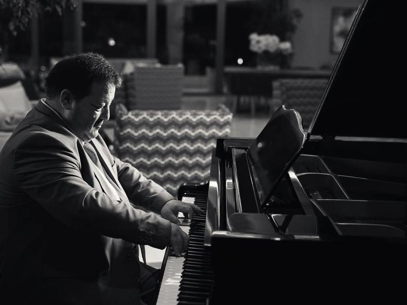 Mann spielt konzentriert Klavier in einem eleganten, gedämpft beleuchteten Raum.