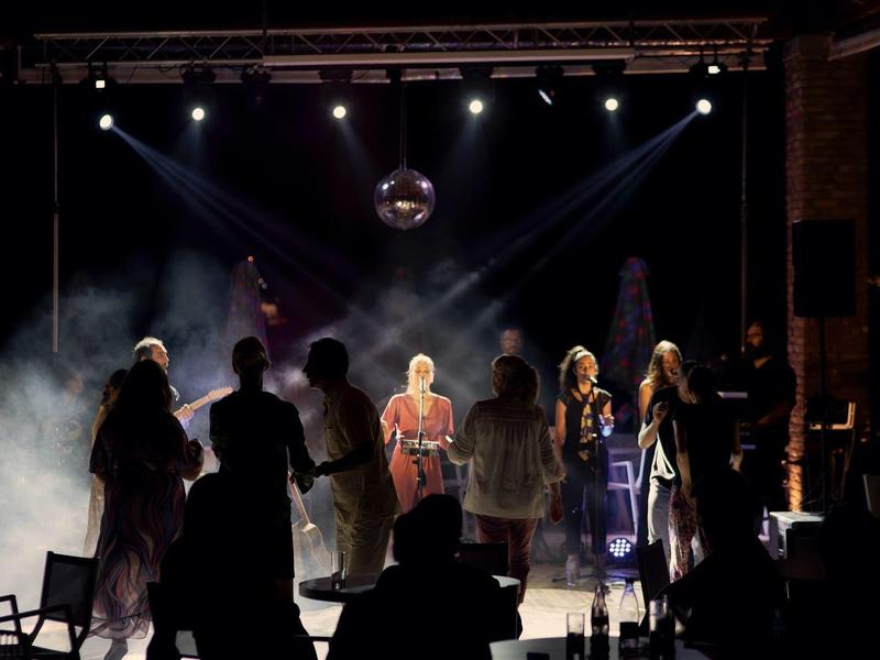 Eine Bühne mit sieben Menschen, dunklem Hintergrund, Nebel und intensiven Scheinwerfern von oben.