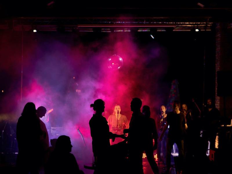 Menschen tanzen in dunklem Raum mit bunter Nebel- und Lichtshow in Rot und Violett.