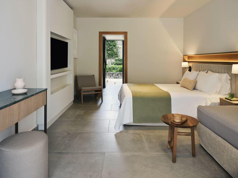 Modernes Hotelzimmer mit großem Bett, Sitzgelegenheiten und Blick auf einen Garten.