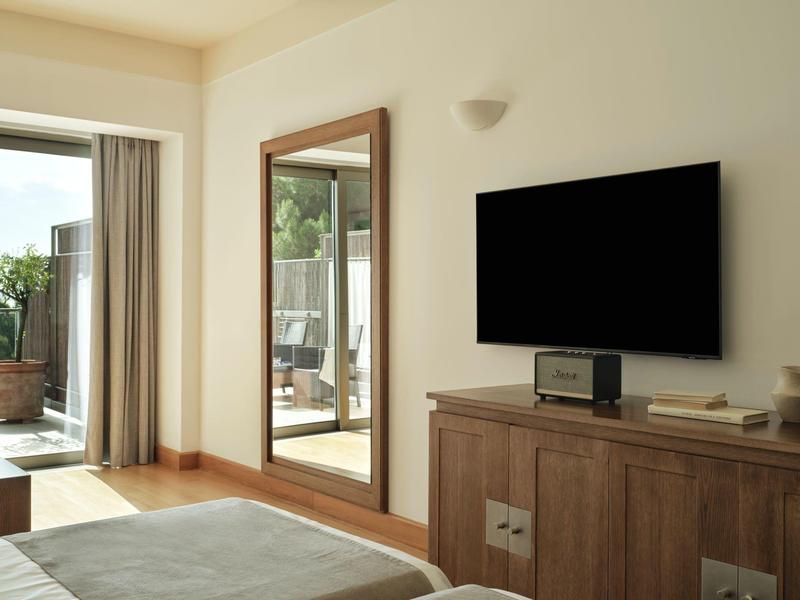 Moderner Hotelzimmerbereich mit großem Spiegel, Flachbildfernseher und Zugang zum Balkon.