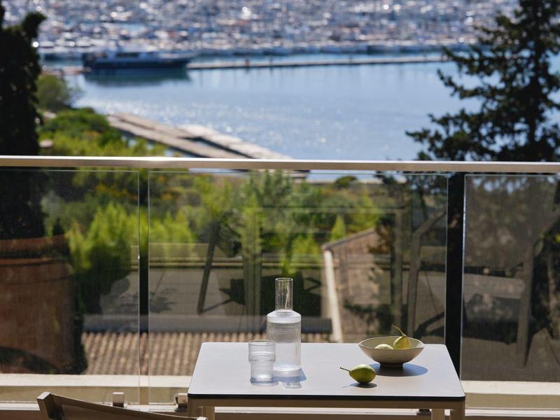 Terrasse mit Tisch und Stühlen, Blick auf einen Hafen mit Booten und Bergen im Hintergrund.