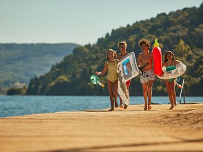 Vier junge Menschen mit aufblasbaren Schwimmringen am Seeufer bei Sonnenschein.