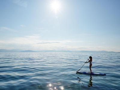 Persona de pie en una tabla de paddle remando en agua azul tranquila bajo un cielo soleado.