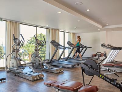 Gimnasio con cintas de correr y equipos de ejercicio junto a grandes ventanas con vista a la vegetación.