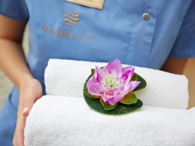 Person hält weiße, gefaltete Handtücher mit einer lilafarbenen Lotusblume darauf.