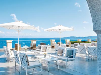 Terraza moderna con muebles blancos y sombrillas con vista al mar azul.