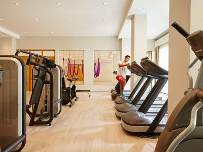 Gimnasio moderno con cintas de correr, máquinas de fuerza y suelo de madera clara.