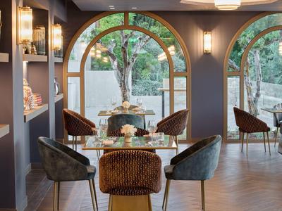 Moderne Sitzecke mit braunen Sesseln, runder Glasplatte und großen Rundbogenfenstern mit Blick ins Grüne.