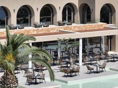 Terrassenrestaurant mit Tischen und Stühlen vor einem Gebäude mit großen Rundbögen.