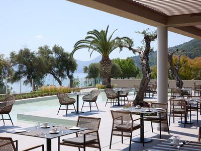 Terraza del hotel con mesas y sillas, palmeras y vista al mar de fondo.