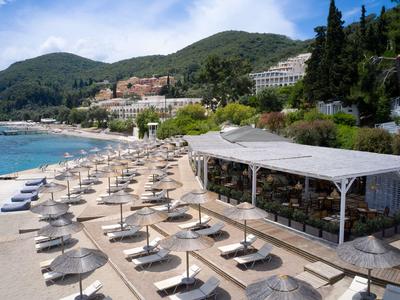 Playa con tumbonas y sombrillas frente a un hotel, rodeada de colinas verdes y cielo despejado.