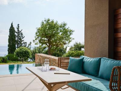 Terrasse mit blauem Sofa, Holztisch, Pool und Blick auf Bäume und Meer im Hintergrund.
