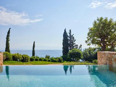 Blick über Pool mit klarem Wasser auf grüne Bäume und blauen Himmel am Meer im Hintergrund.