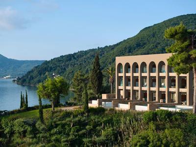 Ein modernes Gebäude mit Rundbögen steht auf einem grünen Hügel mit Blick auf ein blaues Meer.