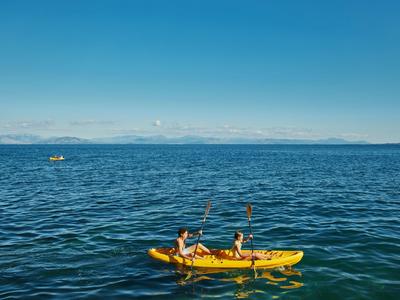 Dos personas reman en un kayak amarillo sobre un mar tranquilo bajo un cielo azul claro.
