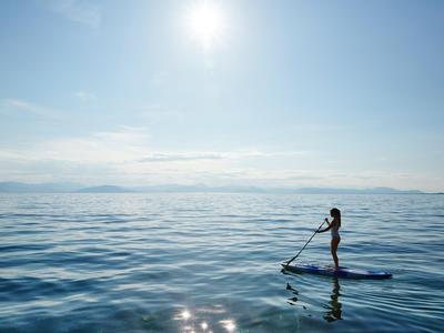 Persona de pie en una tabla de paddle en mar tranquilo bajo cielo despejado.