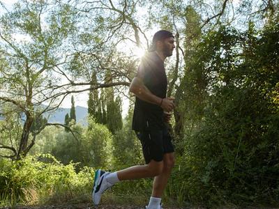 Hombre corriendo por un camino en un área boscosa verde y soleada.