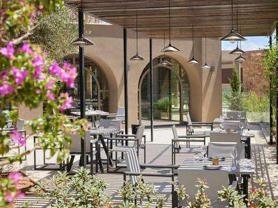 Restaurante al aire libre con mesas y sillas dispuestas bajo un techo de madera y plantas en flor.