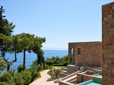 Moderner Steinhaus mit Terrasse, Grünanlage und Blick auf das blaue Meer und den klaren Himmel.