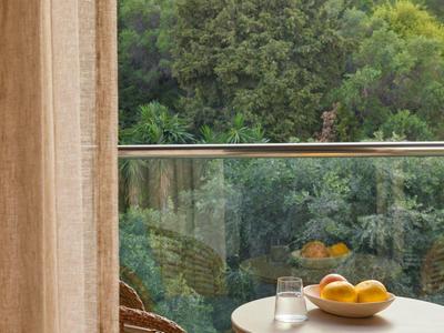 Balkon mit runden Korbstühlen und Tisch, Dose und Schale mit Orangen, grüner Wald im Hintergrund.