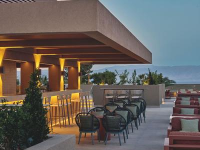 Terraza moderna de hotel con sillas y mesas con vista al mar al atardecer.